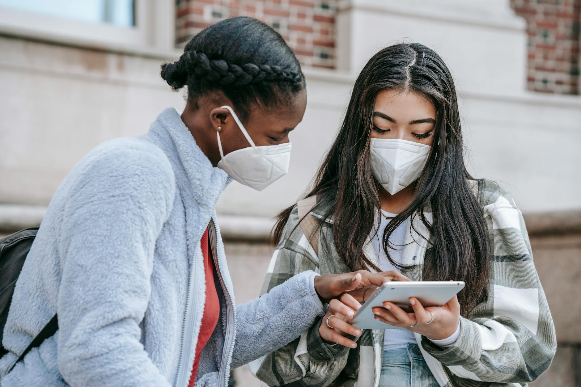 concentrated diverse female students sharing tablet near college building